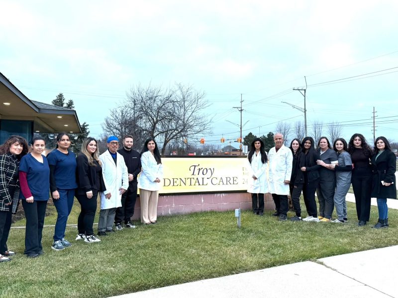 Troy dental care staff standing in front of the clinic surrounding a sign reading, Troy Dental Care.
